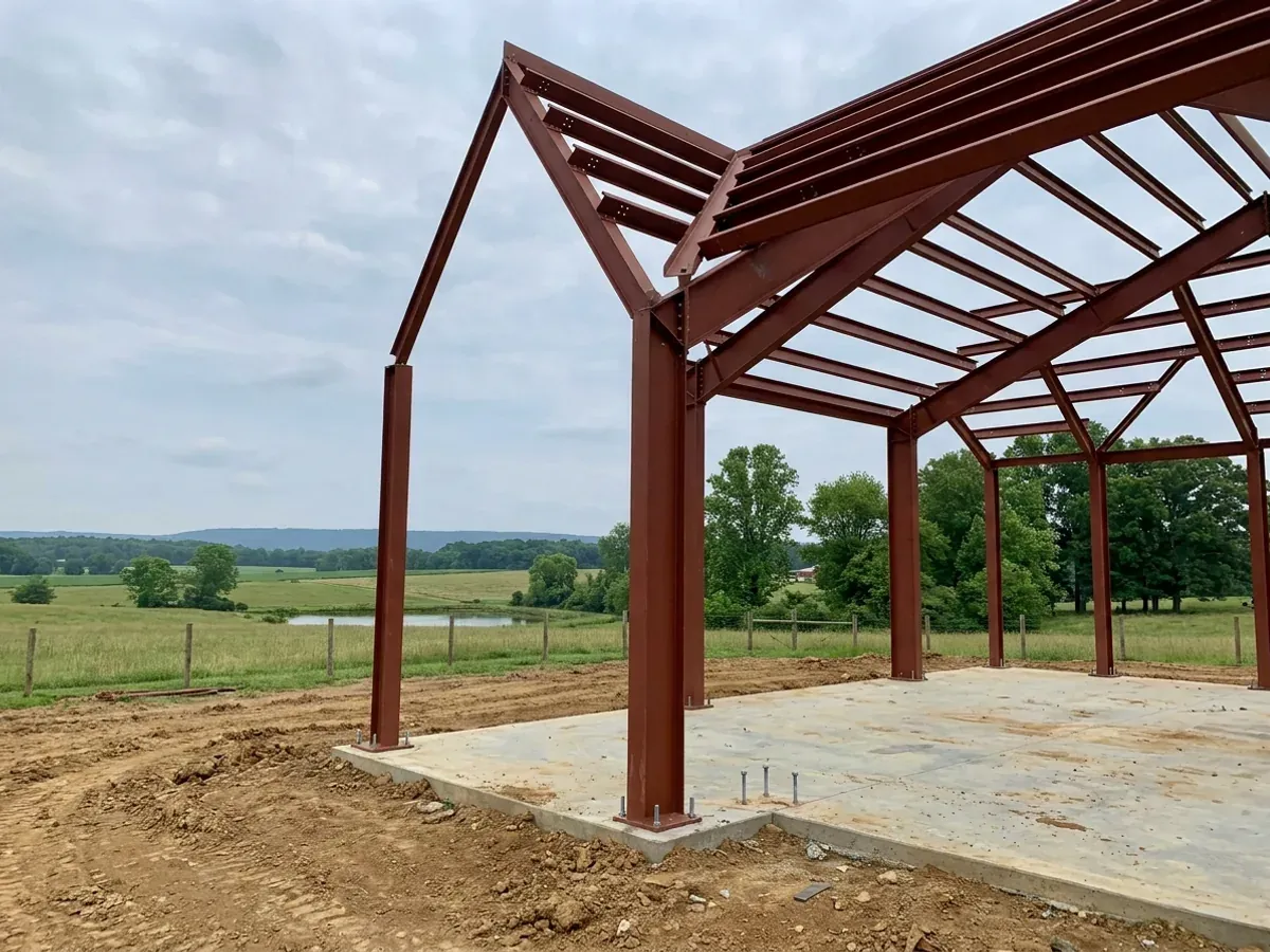 A red oxide primed structural steel frame partly erected on a concrete slab, showing bolted knee joints and anchor bolts.